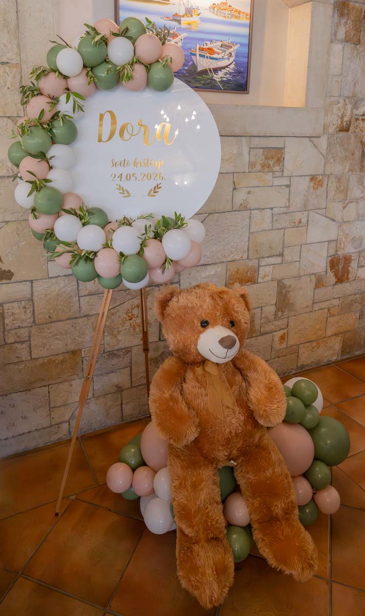 Pastelna dekoracija za sveto krštenje s bijelim, zelenim i pastelno rozim balonima, personaliziranom pločom i plišanim medvjedićem.
